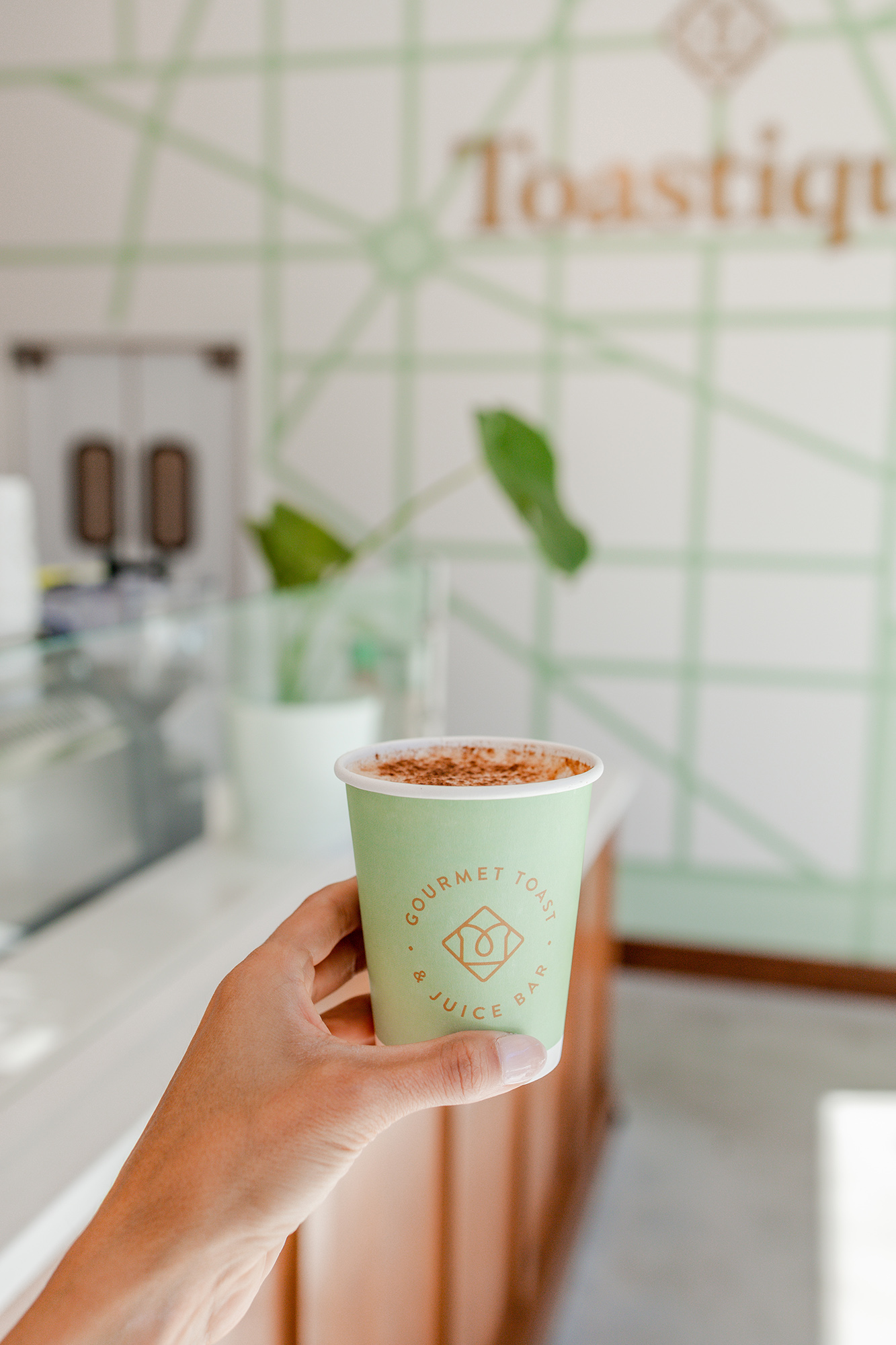 A hand holding a custom printed coffee cup inside a Toastique shop.