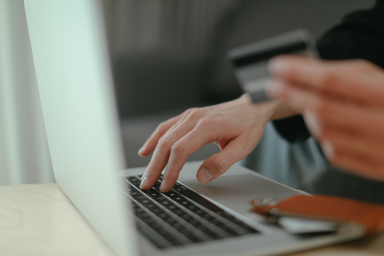 A hand types on a laptop while the other holds a credit card.